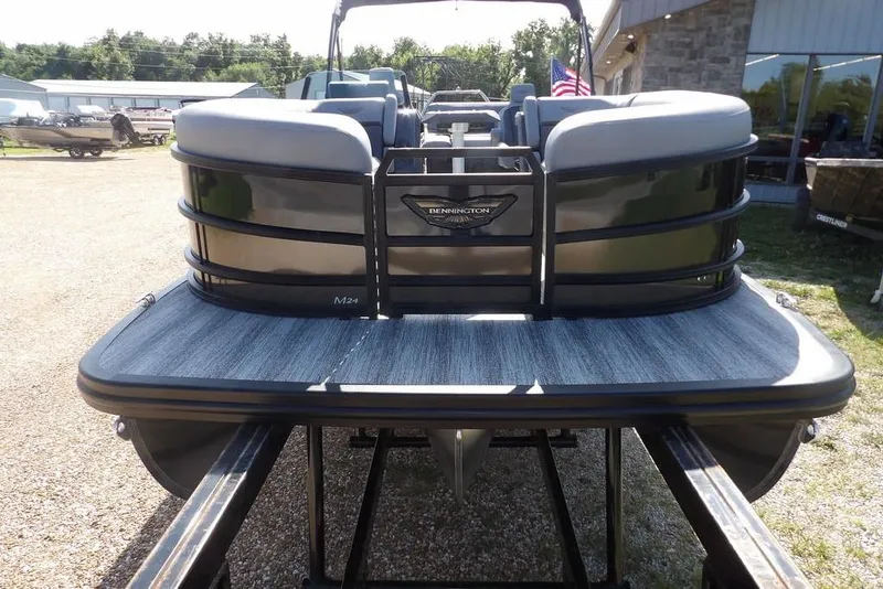 Slide: The Image of 2026 Bennington M Swingback 24 MSB pontoon boat on trailer, American flag in background. - 2