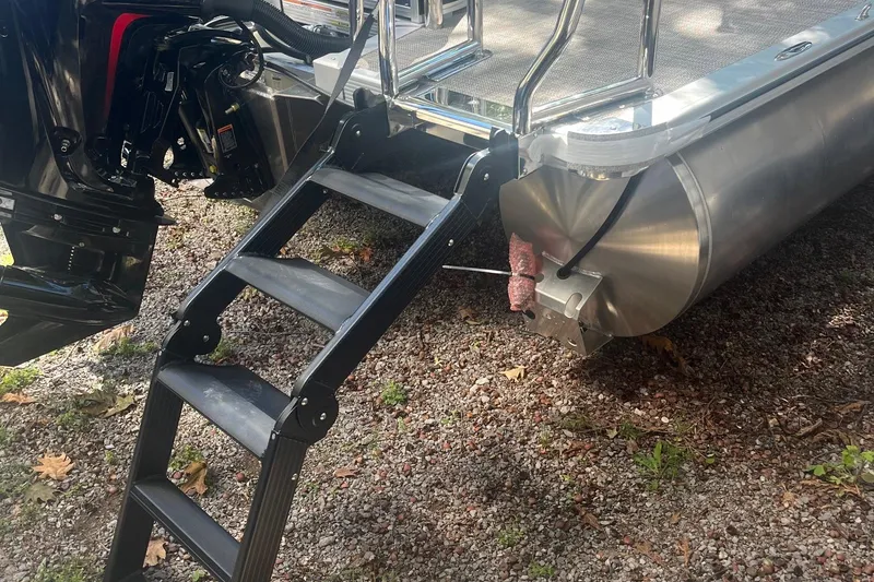 Slide: The Image of 2026 Avalon 25 LSZ Quad Lounger pontoon boat with ladder and motor on gravel. - 6