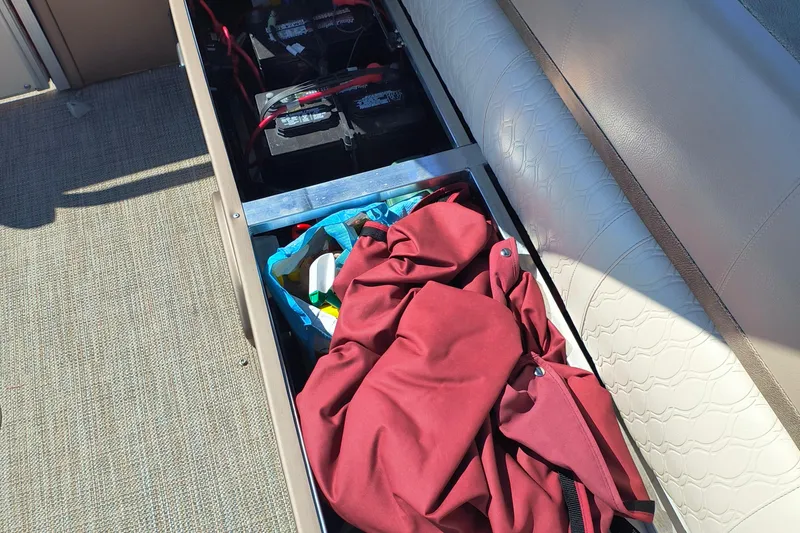 Slide: The Image of Storage compartment of 2022 Avalon Catalina Quad Lounge 25 with batteries and red cover. - 20