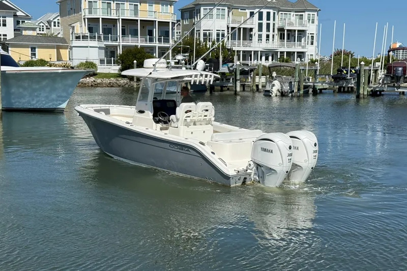 Slide: The Image of 2023 Cobia 280 Center Console boat with twin Yamaha engines in a marina setting. - 2