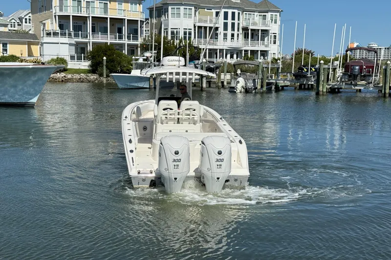 Slide: The Image of 2023 Cobia 280 Center Console boat navigating a marina with waterfront homes. - 4