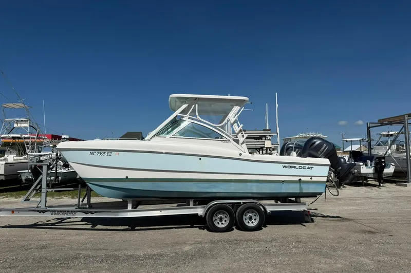 Slide: The Image of 2023 World Cat 230 DC boat on trailer, parked in marina under clear blue sky. - 2