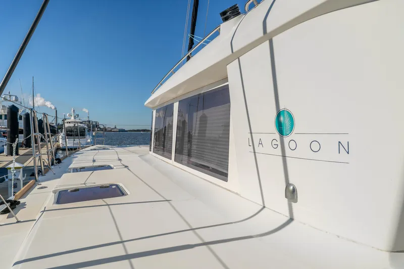 Slide: The Image of 2012 Lagoon 560 yacht docked, showcasing sleek design and spacious deck under clear blue sky. - 13