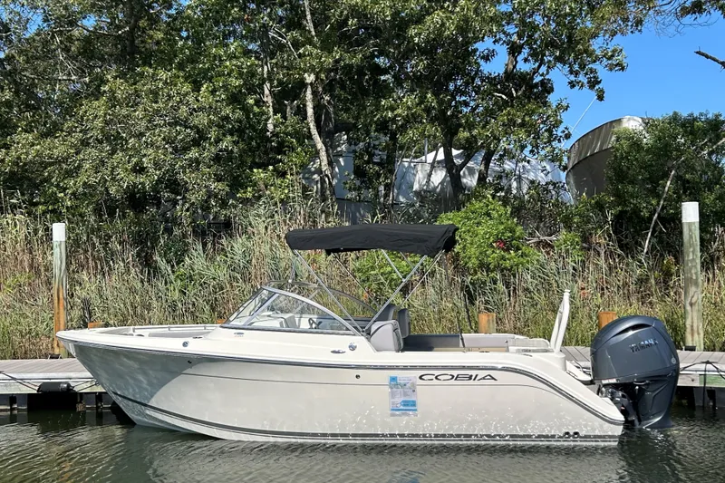 The Image of 2026 Cobia 220 Dual Console boat docked by lush greenery. - 0