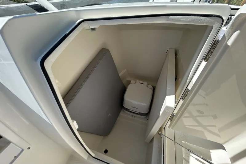 Slide: The Image of 2026 Cobia 220 Dual Console boat interior with portable toilet and storage compartment. - 13