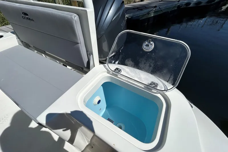 Slide: The Image of 2026 Cobia 220 Dual Console boat with open storage compartment by the water. - 5