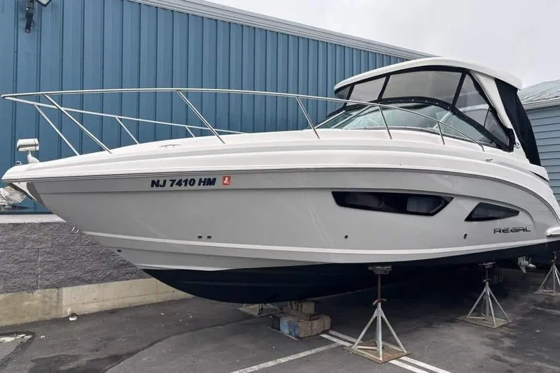 The Image of 2019 Regal 33 XO boat on stands, parked near a blue building. - 0