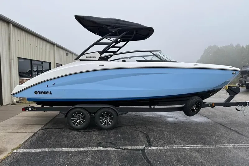 The Image of 2026 Yamaha Boats 252SD on trailer, blue and white design, parked outside a building. - 0