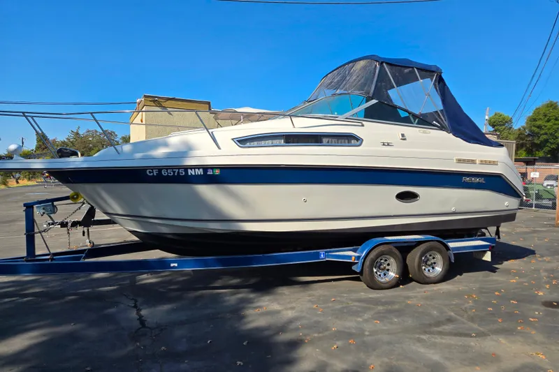 The Image of 1995 Regal Commodore 258 boat on trailer, parked outdoors under clear blue sky. - 1