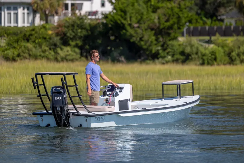 Slide: The Image of Man steering 2018 Xplor X18 boat on calm water near grassy shoreline. - 5