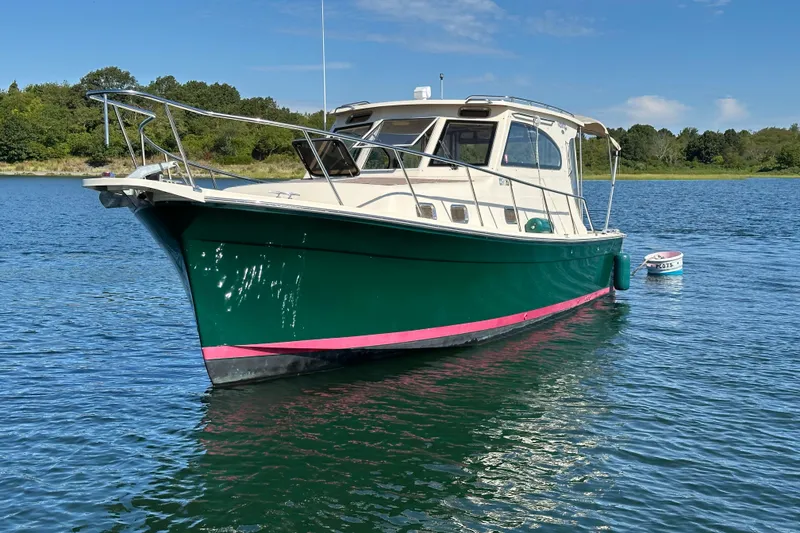 Slide: The Image of 2004 Mainship Pilot 30 boat on calm water, green hull, clear sky background. - 2
