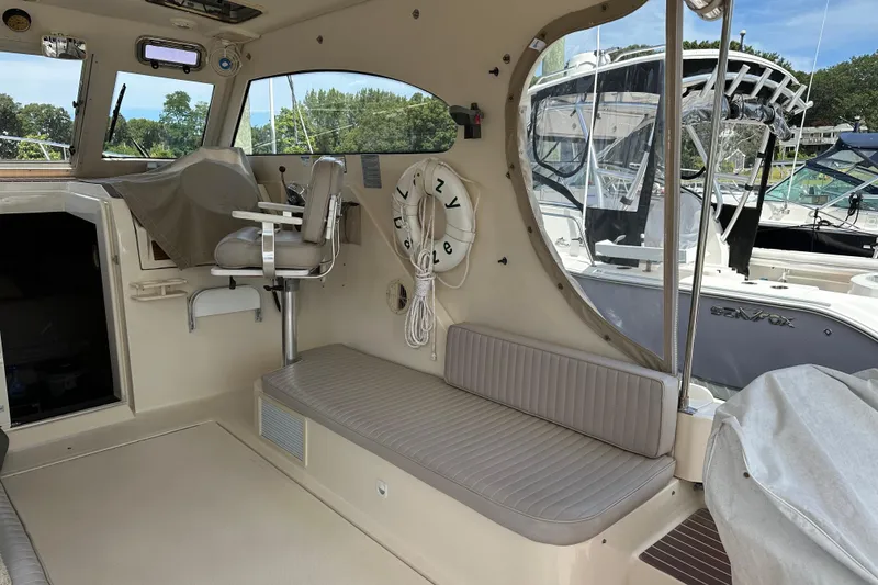 Slide: The Image of 2004 Mainship Pilot 30 interior with seating, helm chair, and docked boats in background. - 9