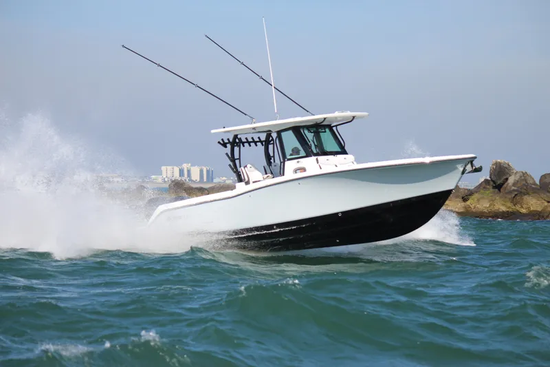 Slide: The Image of 2023 Crevalle 33 CSF boat navigating through waves near rocky shoreline. - 2