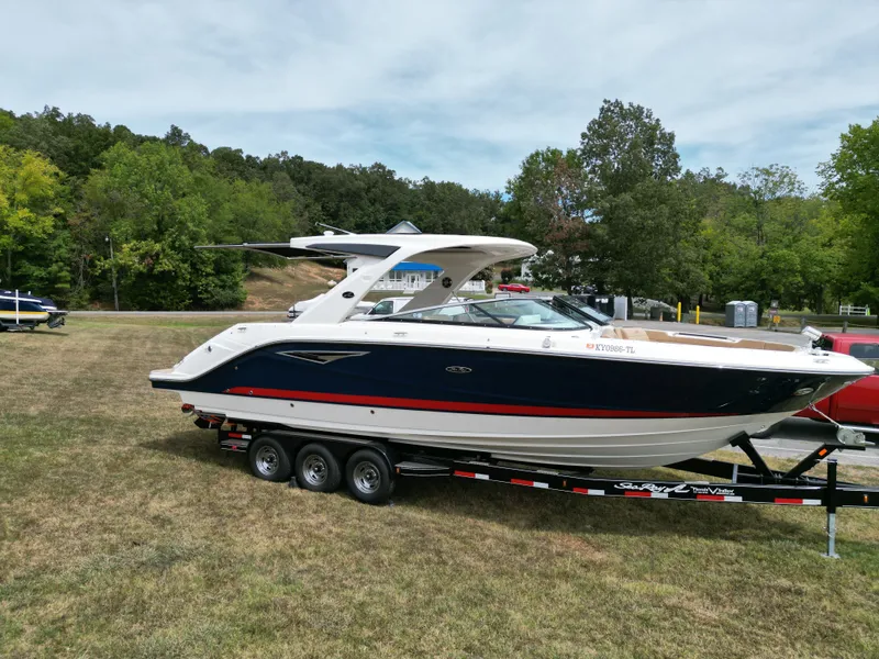 Slide: The Image of 2022 Sea Ray SLX 310 boat on trailer, parked on grass with trees in background. - 2
