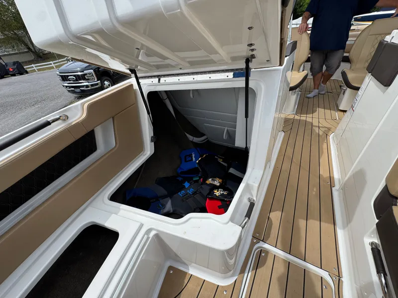 Slide: The Image of 2022 Sea Ray SLX 310 boat storage compartment with life jackets, open hatch, and teak flooring. - 47