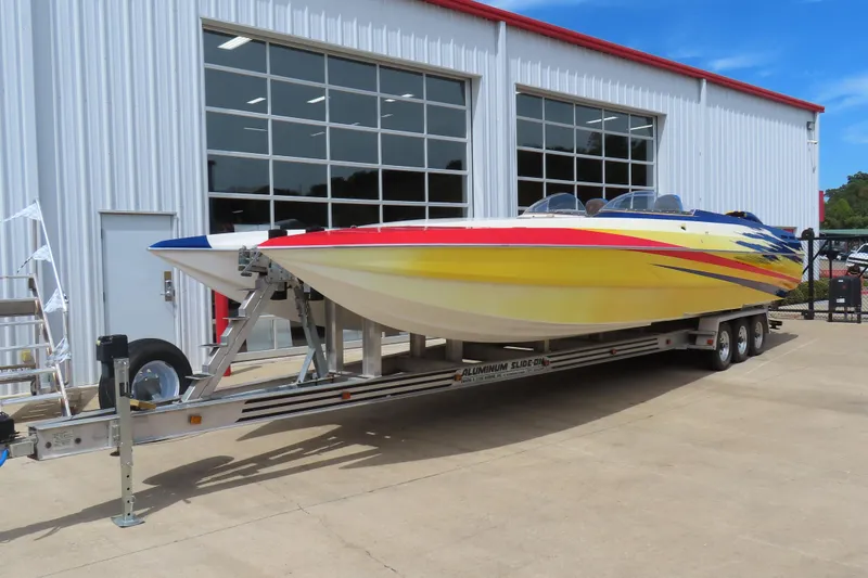 Slide: The Image of 2003 Spectre 36 Cat powerboat on trailer, vibrant yellow and red design, parked outside a garage. - 2