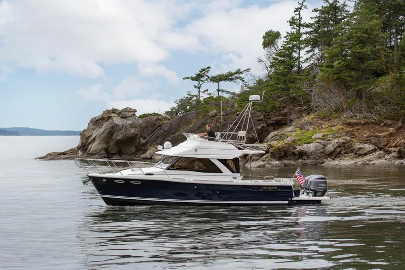 Slide: The Image of 2026 Cutwater C-32 CB boat cruising near rocky shoreline with trees. - 10