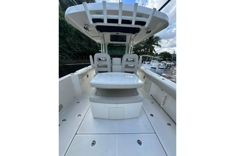 Slide: The Image of 2022 Boston Whaler 330 Outrage boat interior with seating and table, docked outdoors. - 12