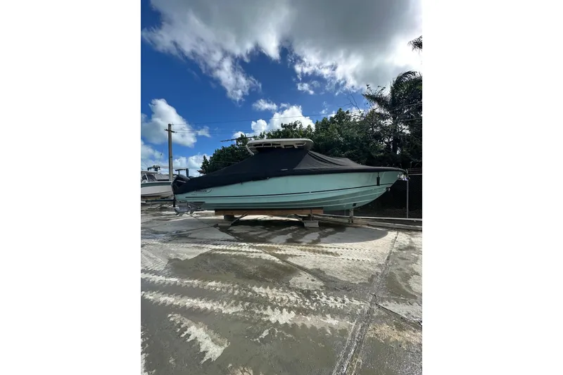 Slide: The Image of 2022 Boston Whaler 330 Outrage boat covered, parked outdoors under a cloudy sky. - 4