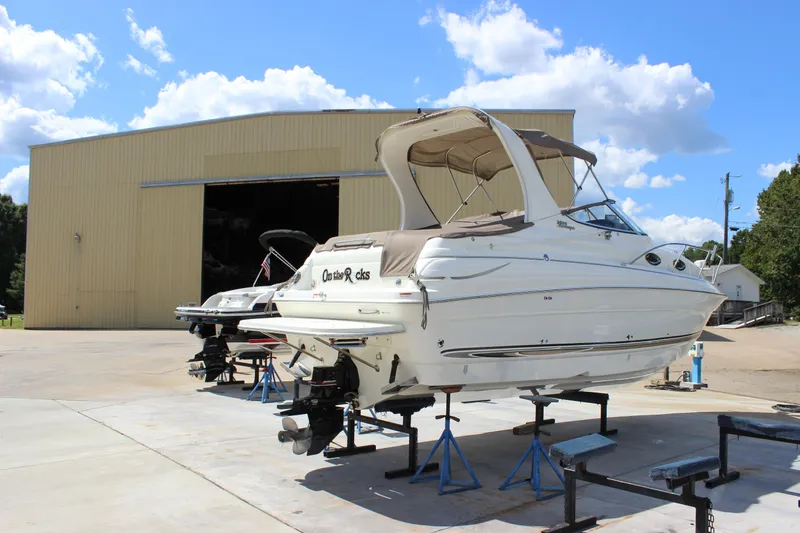 The Image of 2003 Wellcraft Martinique 2600 boat on stands outside a large storage facility. - 1