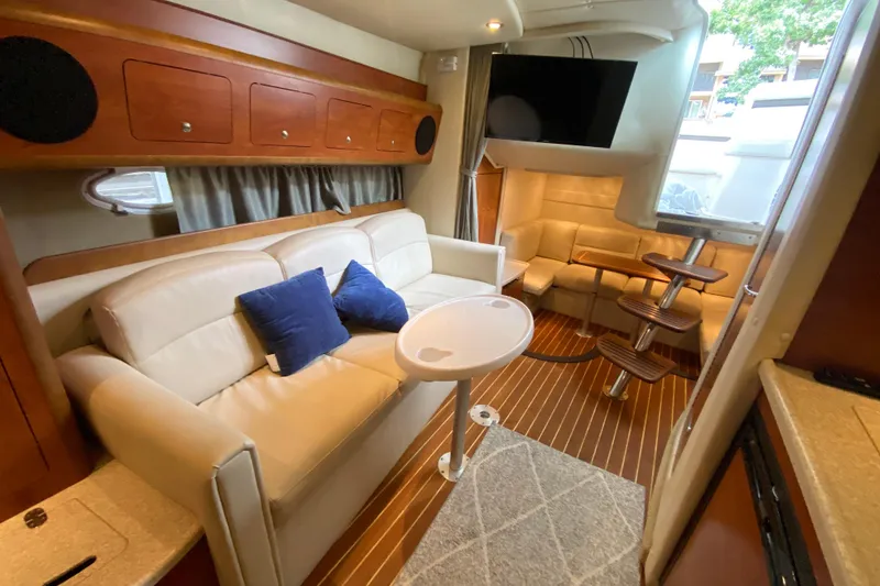 Slide: The Image of 2008 Rinker 350 Express Cruiser interior with beige seating, wooden accents, and a mounted TV. - 29