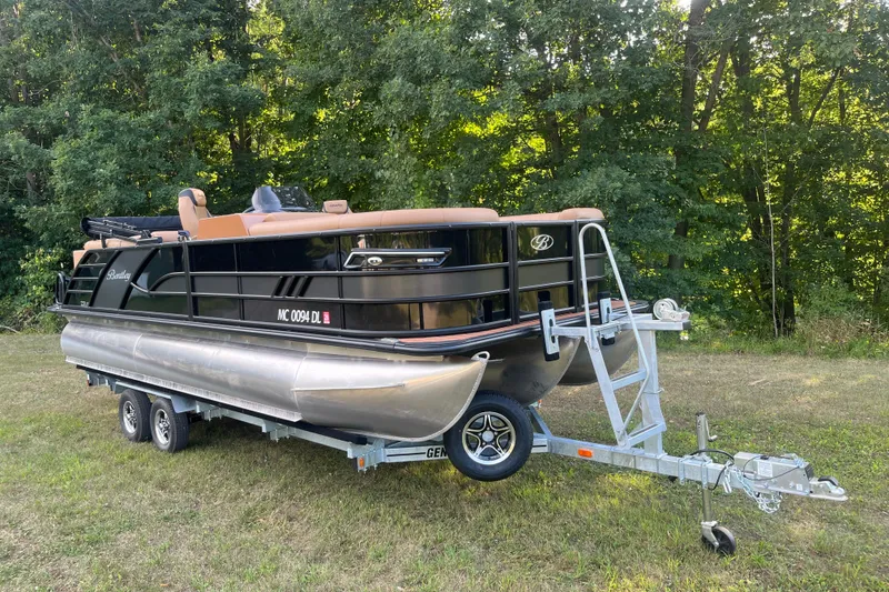 Slide: The Image of 2025 Bentley Pontoons 220/223 Elite Admiral on trailer, parked on grass with forest backdrop. - 1