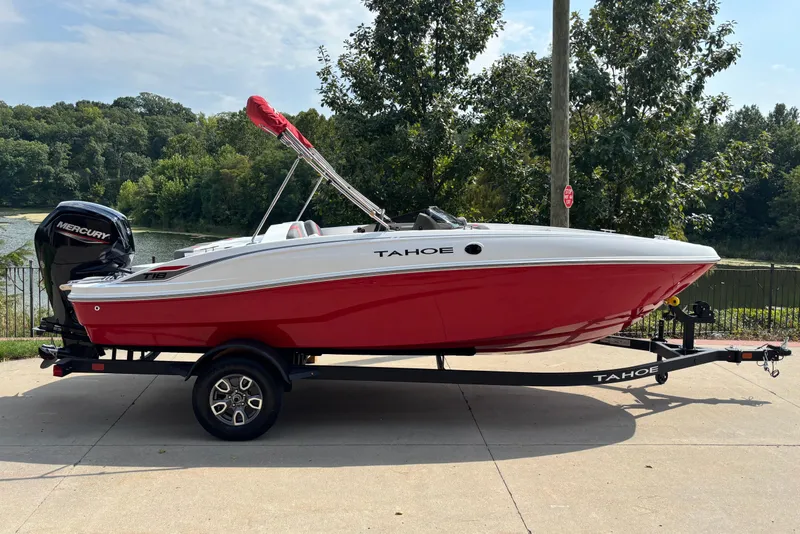 The Image of 2026 Tahoe T18 boat with red hull on trailer, parked near a scenic lake. - 0