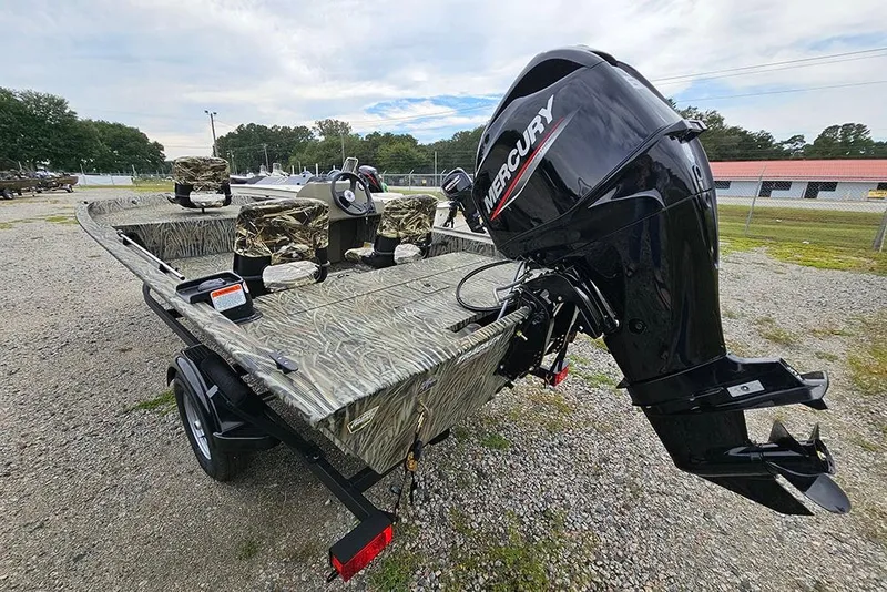 Slide: The Image of 2026 Tracker Grizzly 1754 SC boat with Mercury outboard motor, camo seats, parked on gravel. - 7