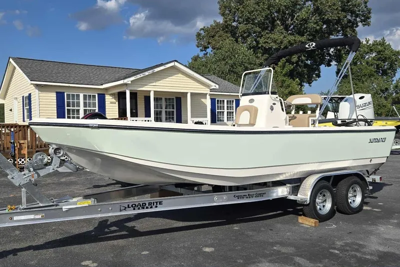 The Image of 2026 Sundance DX22 boat on trailer, parked near a house under a clear sky. - 1