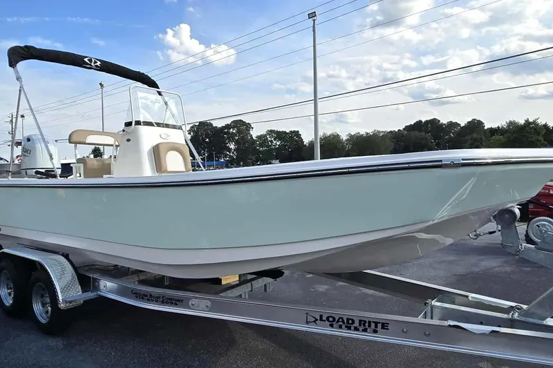 Slide: The Image of 2026 Sundance DX22 boat on trailer under blue sky, side view. - 6