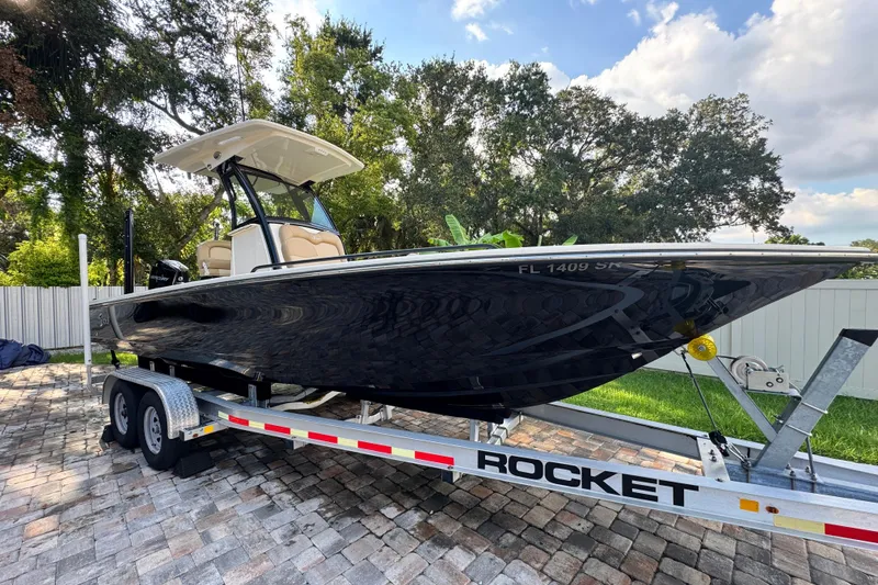 Slide: The Image of 2020 Scout 251 XSS boat on trailer, parked on paved driveway, surrounded by trees. - 1