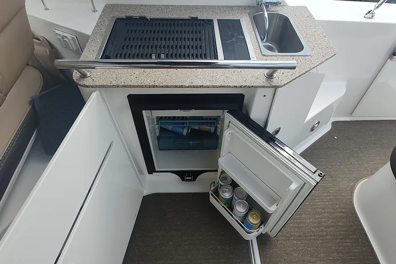 Slide: The Image of 2017 Sea Ray Sundancer 310 boat kitchenette with grill, sink, and open mini fridge. - 18
