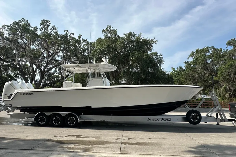 Slide: The Image of 2024 Contender 39 ST boat on trailer, parked in a lot under cloudy sky. - 14