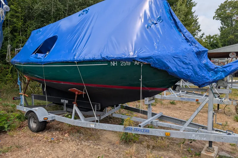 The Image of 1981 Cape Dory Typhoon sailboat on trailer, covered with blue tarp, parked outdoors. - 0
