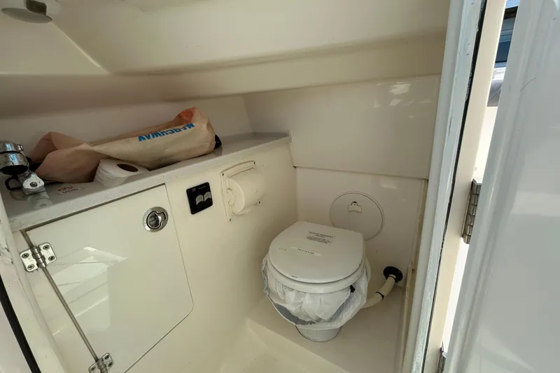 Slide: The Image of 2022 Cobia 240 Dual Console boat interior with compact marine toilet and storage. - 7