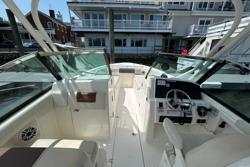 Slide: The Image of 2022 Cobia 240 Dual Console boat interior with steering wheel and seating, docked near buildings. - 8