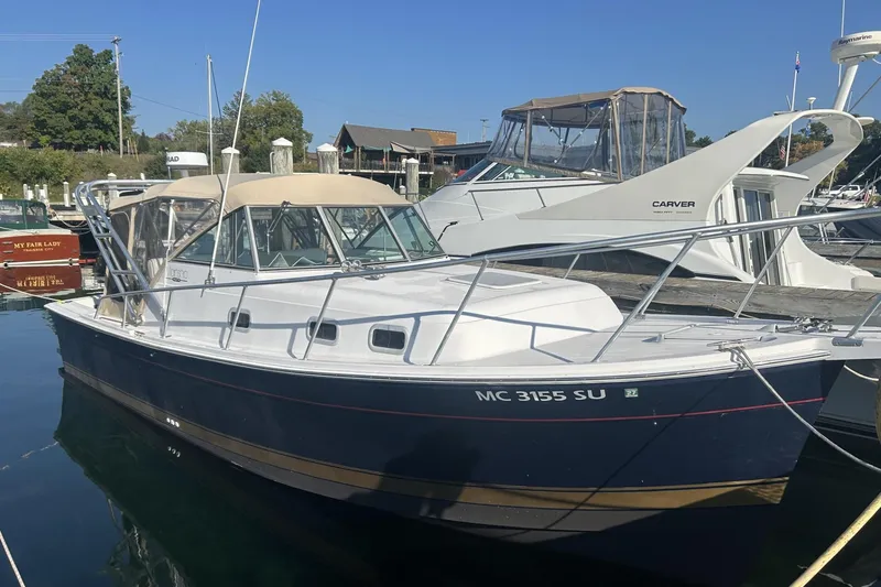 The Image of 1998 Mainship Pilot 30 boat docked in a marina, featuring a blue hull and beige canopy. - 1