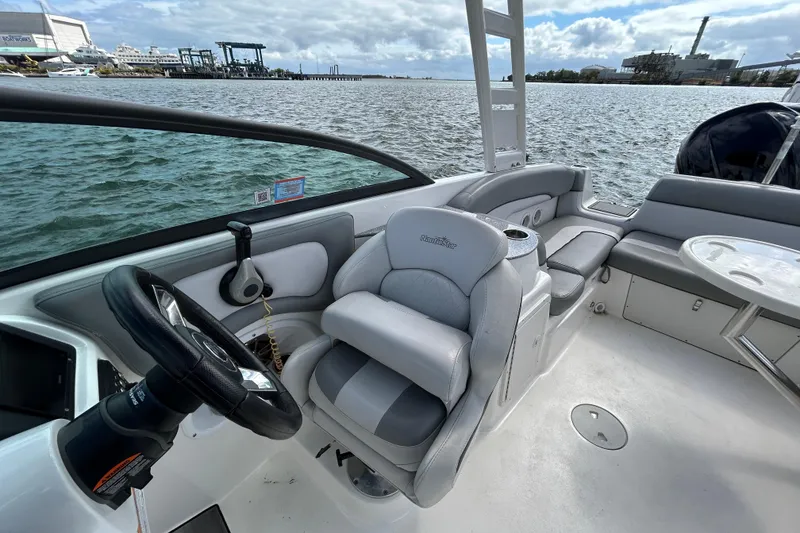 Slide: The Image of 2022 NauticStar 243 DC boat interior with steering wheel and seating, docked by the water. - 11