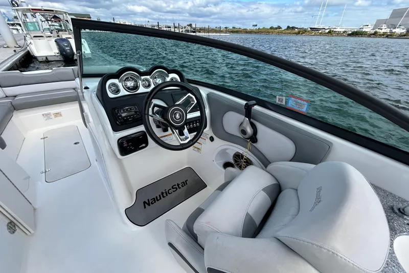 Slide: The Image of 2022 NauticStar 243 DC boat interior with steering wheel and dashboard, docked by the water. - 9