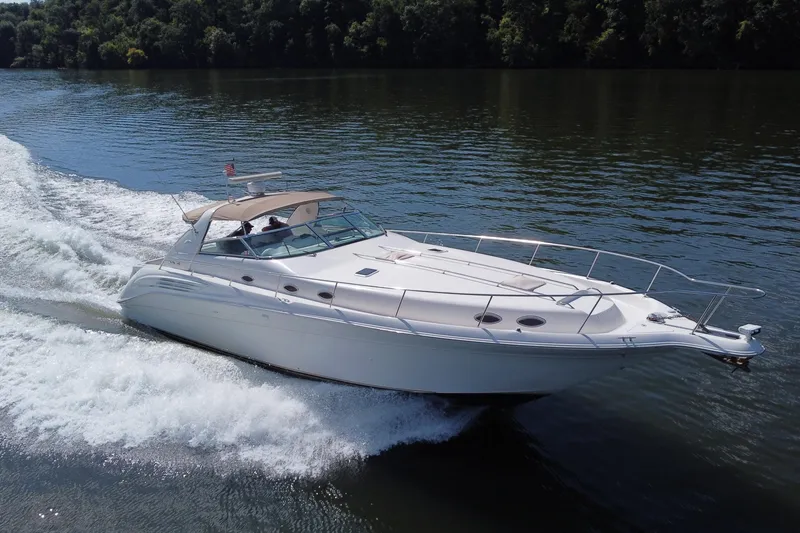 The Image of 1997 Sea Ray 450 Sundancer cruising on a calm lake, surrounded by lush greenery. - 0