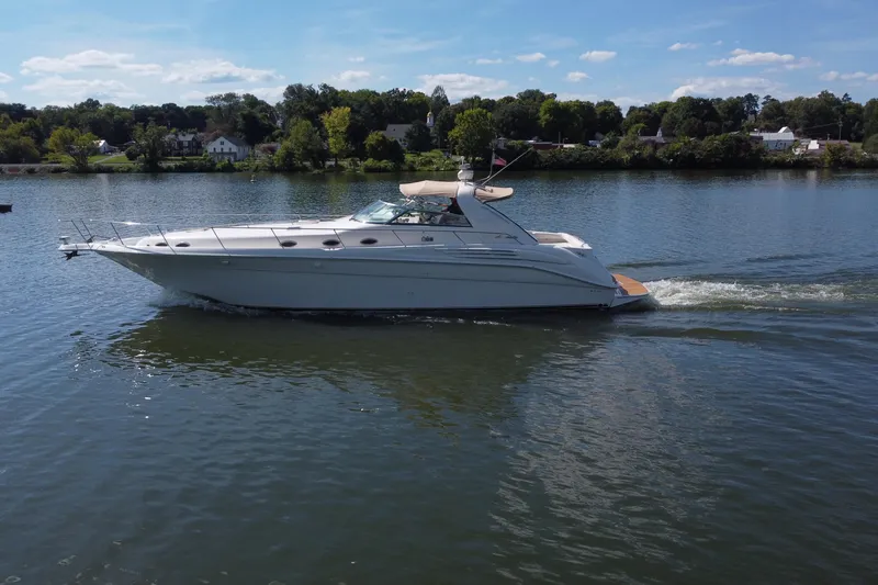 Slide: The Image of 1997 Sea Ray 450 Sundancer cruising on a calm lake under a clear blue sky. - 12