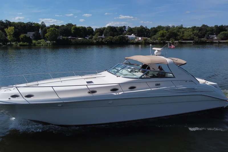 Slide: The Image of 1997 Sea Ray 450 Sundancer cruising on a serene lake under a clear blue sky. - 13