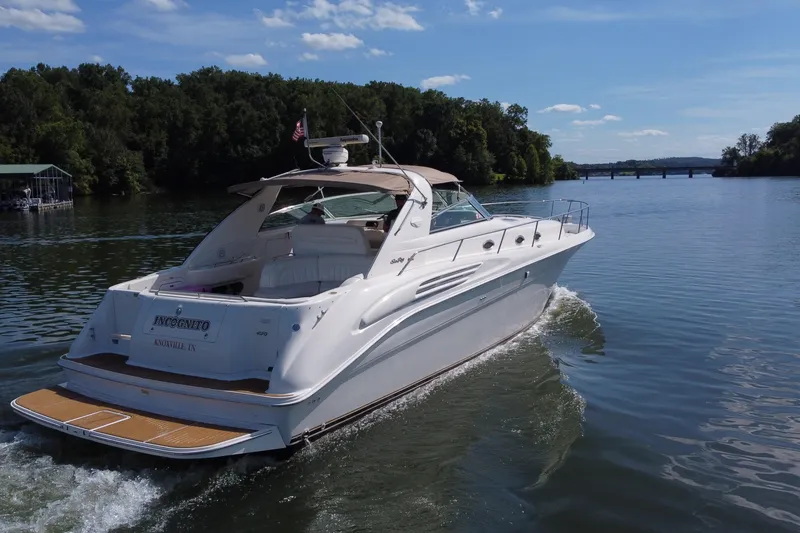 Slide: The Image of 1997 Sea Ray 450 Sundancer cruising on a scenic river under a clear blue sky. - 19