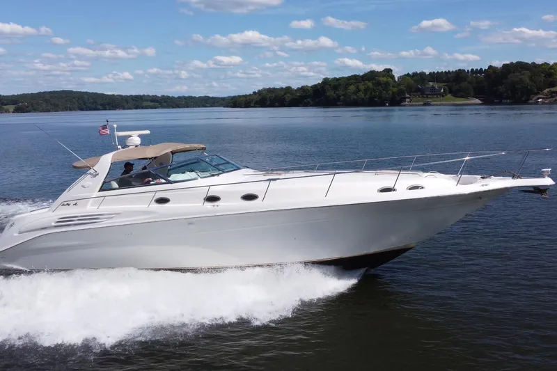Slide: The Image of 1997 Sea Ray 450 Sundancer cruising on a serene lake under a clear blue sky. - 2