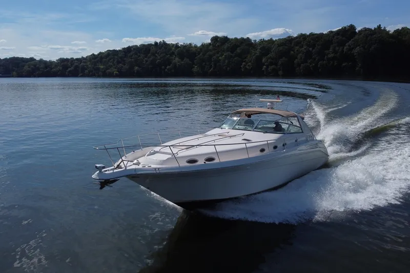 Slide: The Image of 1997 Sea Ray 450 Sundancer cruising on a serene lake with lush forest backdrop. - 20