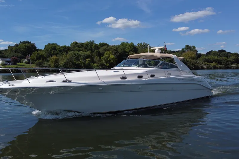 Slide: The Image of 1997 Sea Ray 450 Sundancer cruising on a serene lake under a clear blue sky. - 25