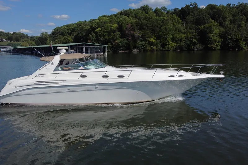 Slide: The Image of 1997 Sea Ray 450 Sundancer cruising on a serene lake with lush green shoreline. - 26