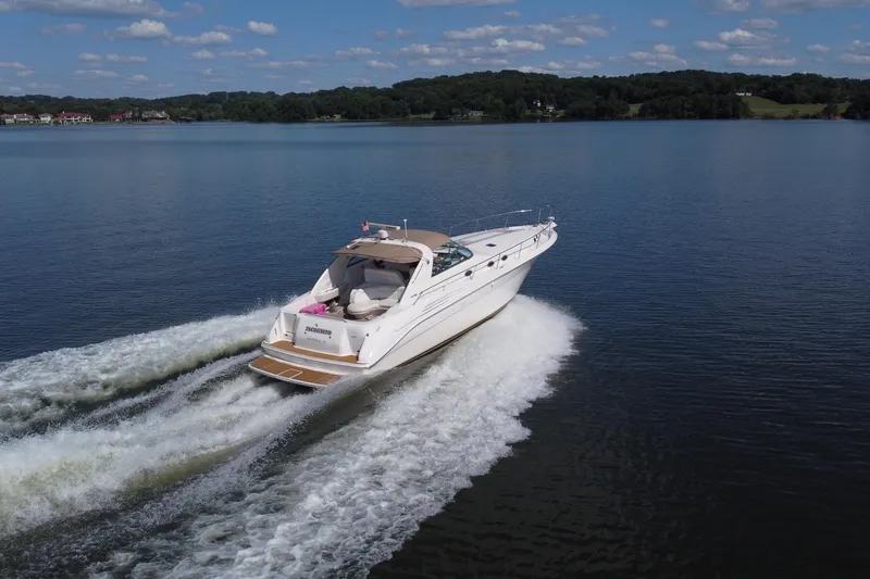 Slide: The Image of 1997 Sea Ray 450 Sundancer cruising on a serene lake under a clear blue sky. - 4