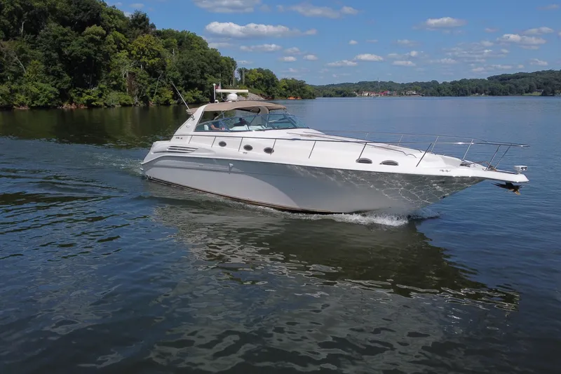 Slide: The Image of 1997 Sea Ray 450 Sundancer cruising on a serene lake under a clear blue sky. - 6