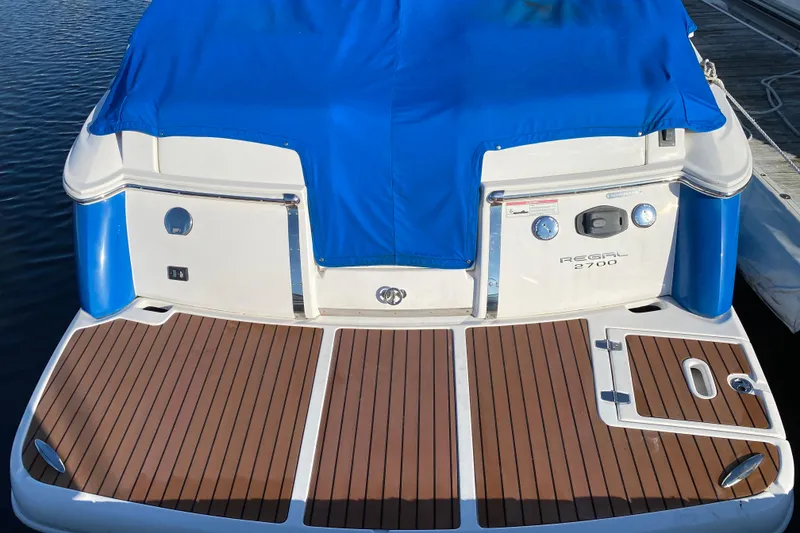 Slide: The Image of 2010 Regal 2700 ES Bowrider with blue cover, parked near coastal homes. - 6